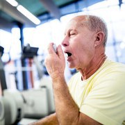 MODEL RELEASED. Senior man using asthma inhaler in gym.