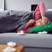Sick woman holding her head while lying in bed under blanket