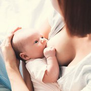 Mother breastfeeding baby in her arms at home. Beautiful mom breast feeding her newborn child. Baby eating mother's milk. Young woman nursing and feeding baby. Concept of lactation infant.