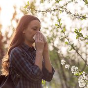 Young pretty girl blowing nose in front of blooming tree. Spring allergy concept