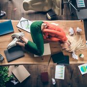 High angle above view photo of corporate messy atmosphere unorganized, blond business lady lying table suffering period pms holding hurt belly wear casual outfit indoors