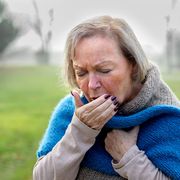 Elderly stylish attractive blond woman coughing or sneezing into her hand as she stands on a rural lane on a misty winter day; Shutterstock ID 529047286; purchase_order: 07-10037-00007; job: -; client: Chiesi; other: Aileen Kaya