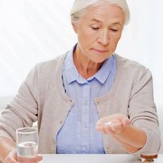 age, medicine, health care and people concept - senior woman with pills and glass of water at home