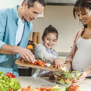 glücklich lächelnde Familie, die gemeinsam in der Küche Salat zubereitet 